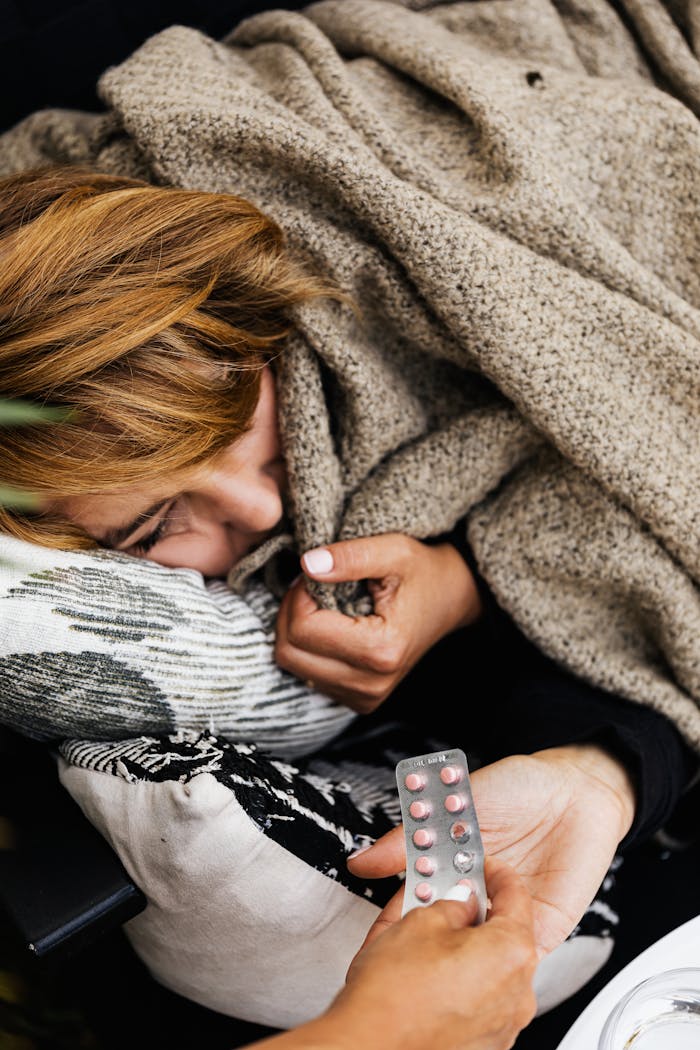 A woman wrapped in a blanket receiving medication while resting at home.